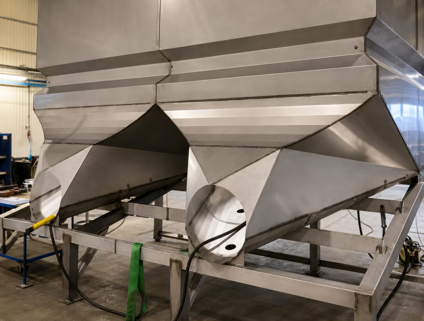 Fabricated stainless steel hopper sections on a support frame in the workshop
